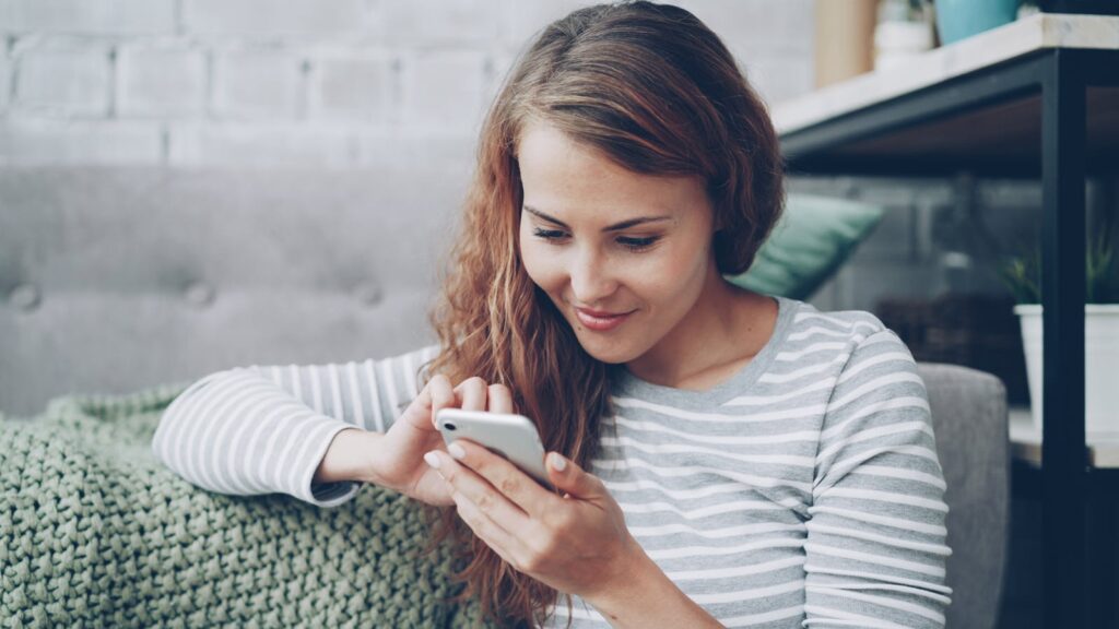 Young woman in casual attire using smartphone, sitting indoors comfortably.