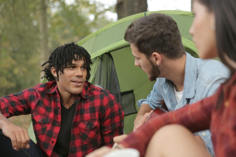A group of diverse friends talking and enjoying a camping trip in nature.