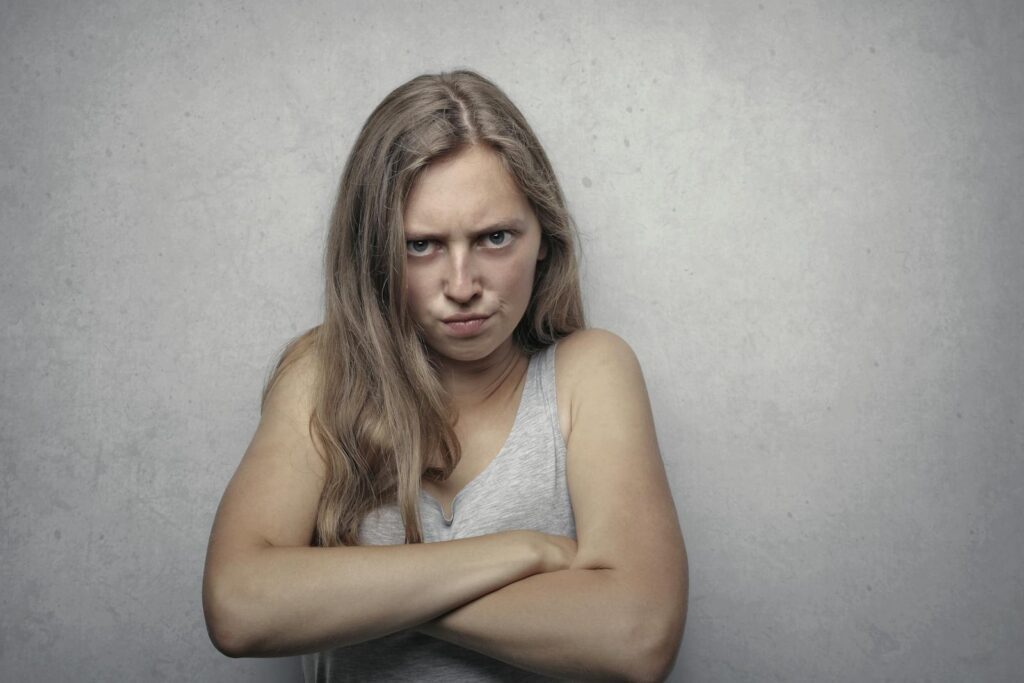 A woman with arms crossed showing a fierce expression against a gray background.