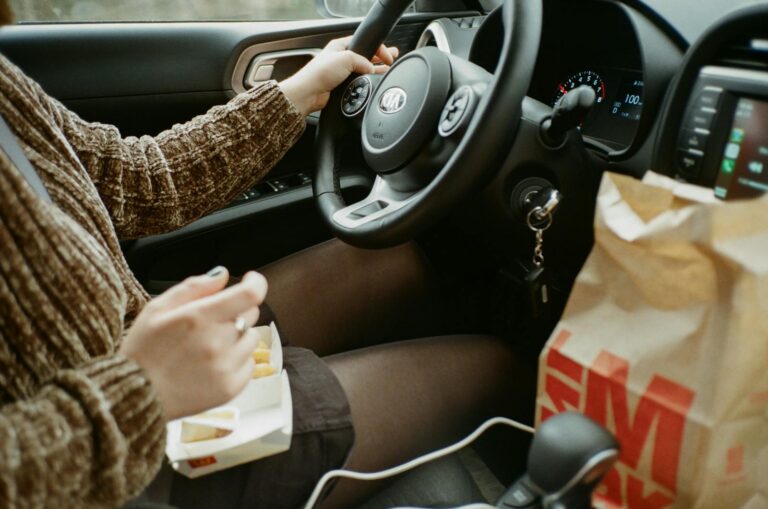 A woman enjoys fast food while driving a Kia on a road trip, showcasing car interior details.