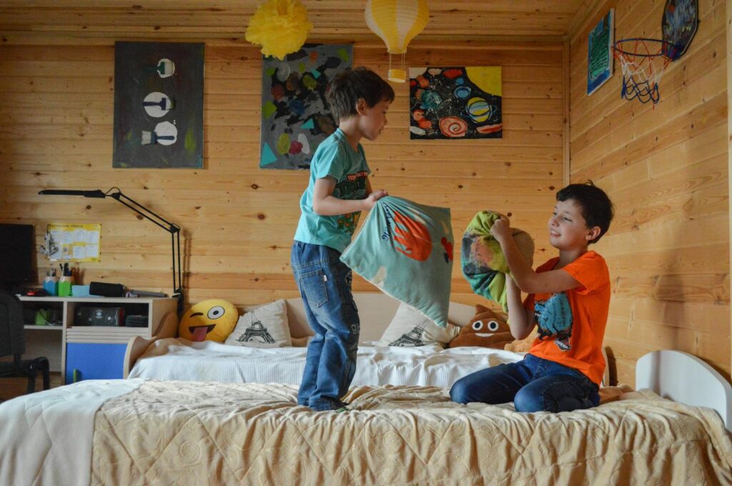 Two boys having fun indoors with a playful pillow fight in a cozy wooden room.