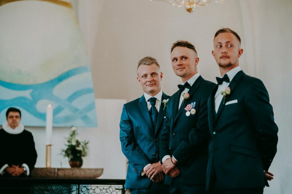Elegant groomsmen in blue suits standing confidently at an indoor wedding ceremony.