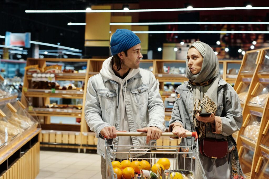 A diverse couple shopping for groceries in a supermarket aisle with a cart full of fruits.