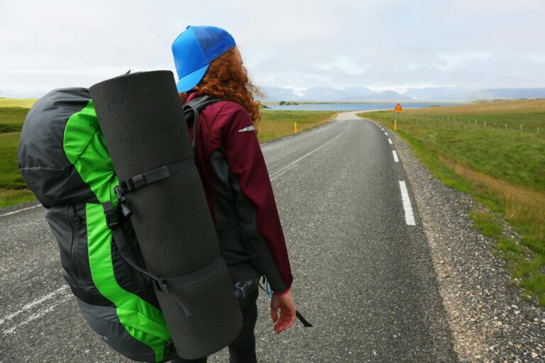 Traveler with backpack walks down an open Icelandic road, ready for adventure.