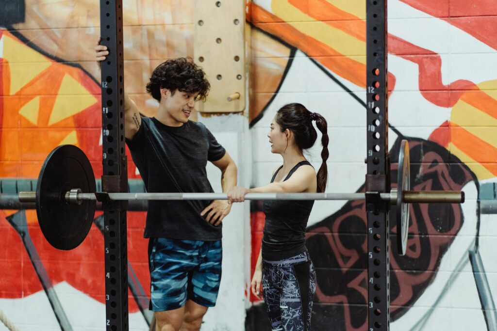 A man and woman talking near gym equipment with colorful graffiti background.