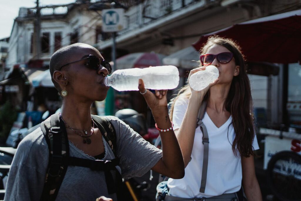 Two women quenching their thirst with bottled water during a sunny outdoor adventure.