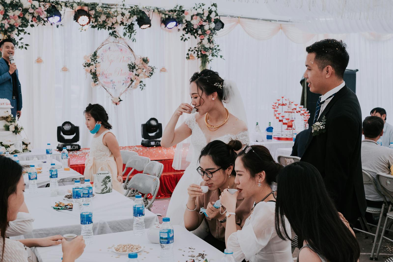 Young ethnic bride with groom and guests in elegant tent drinking together while toasting