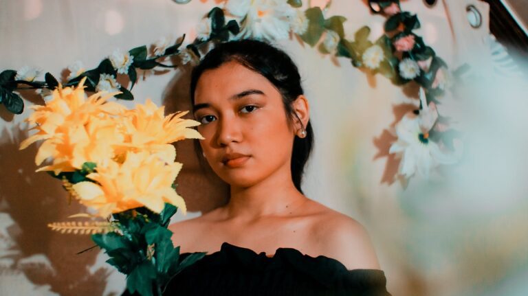 A serene portrait of a woman posing with vibrant yellow artificial flowers indoors.