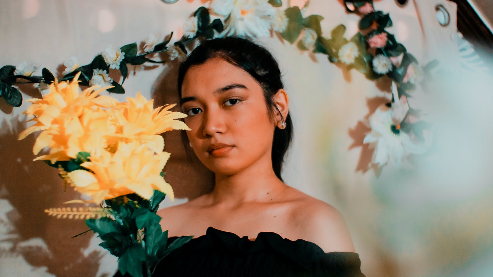 A serene portrait of a woman posing with vibrant yellow artificial flowers indoors.
