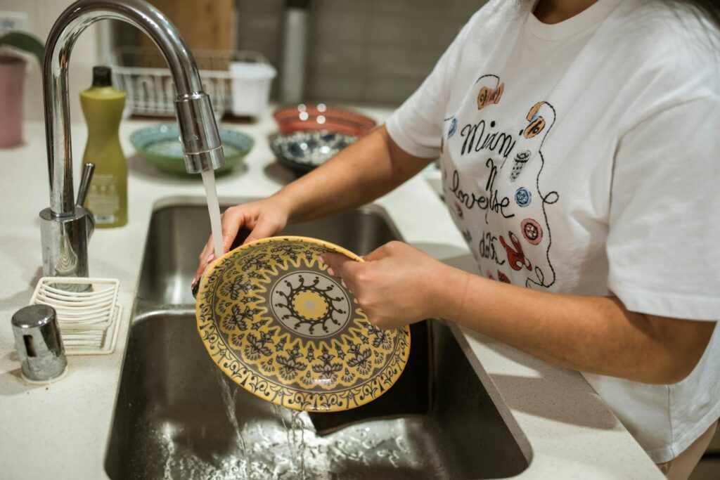 Close-up of hands washing a decorative plate in a modern kitchen sink.