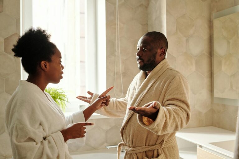 A couple in bathrobes having a discussion in a bathroom setting, expressing emotions.
