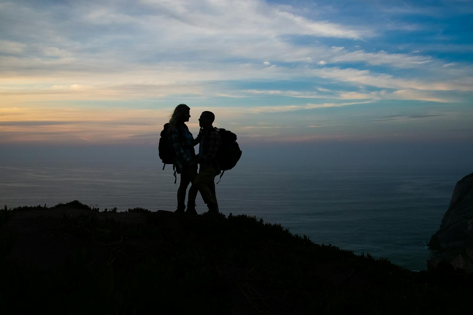 Romantic silhouette of a couple of backpackers enjoying the ocean view at sunset in Portugal.