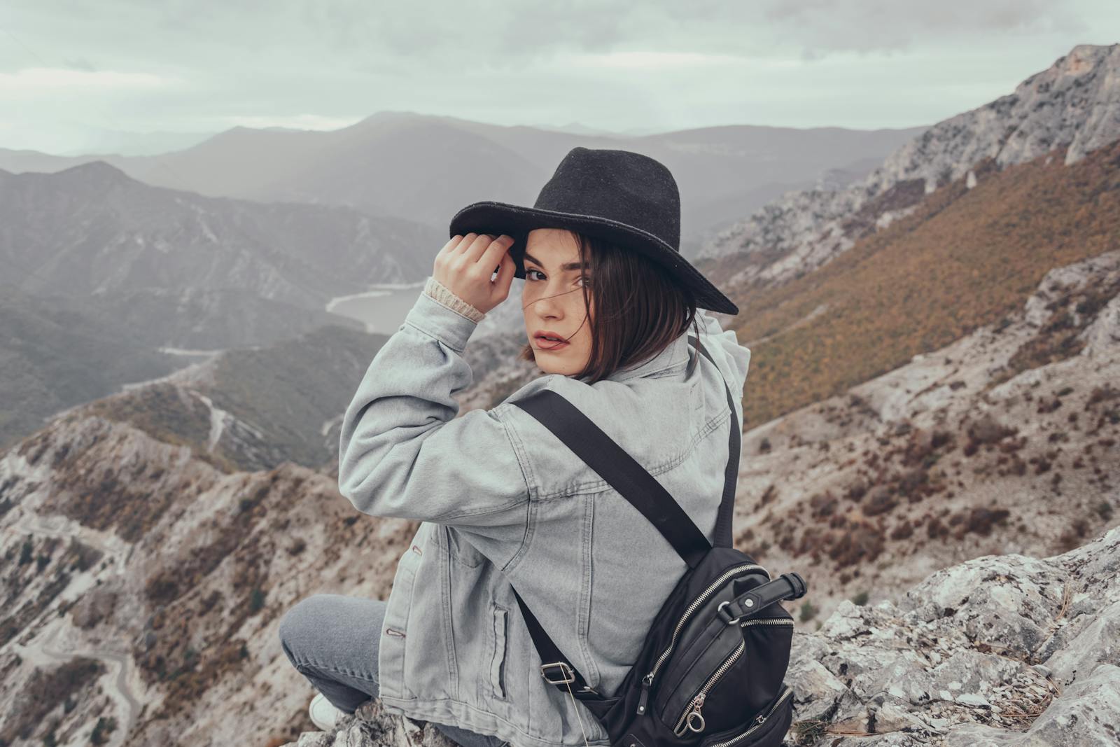 Young woman in denim and hat enjoying a mountain top view, capturing wanderlust and adventure.