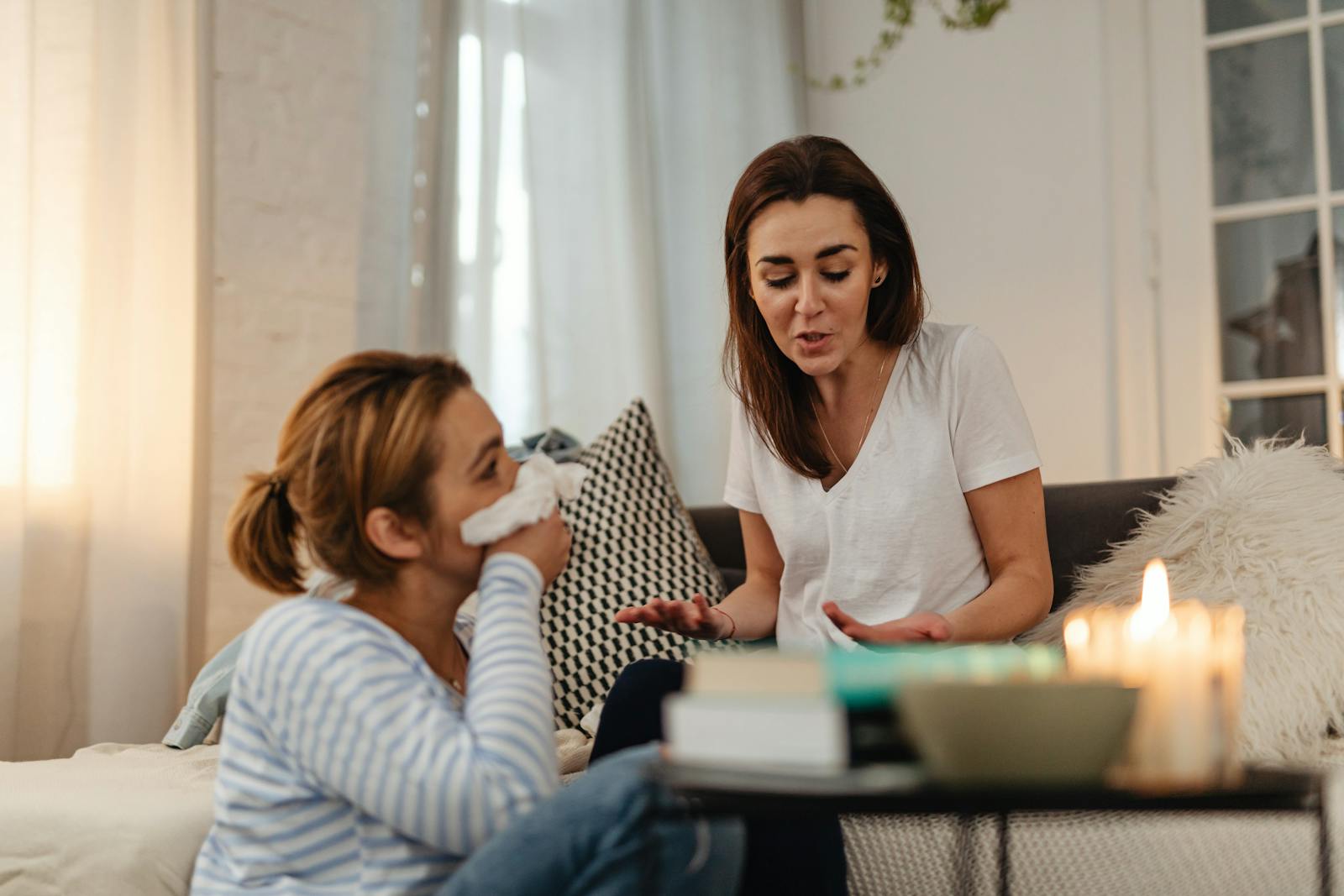 Two women engage in a heartfelt conversation, indoors, with candles creating a cozy atmosphere.