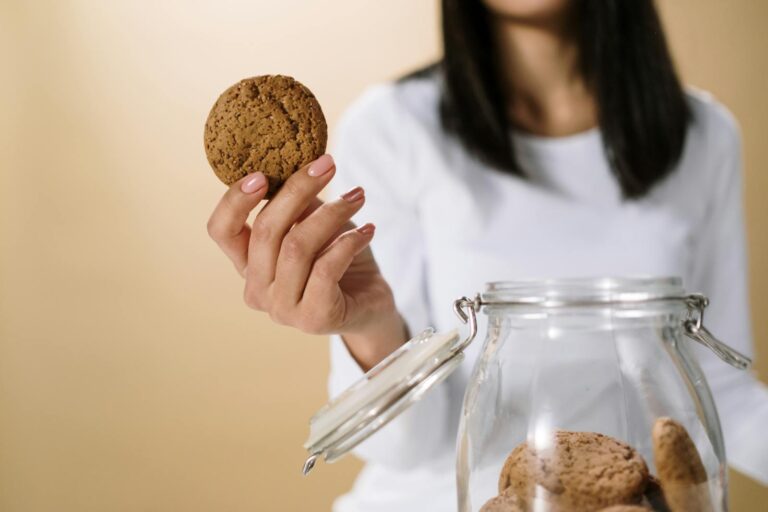 Close-up of a woman's hand holding a cookie from a glass jar, with a soft focus background.