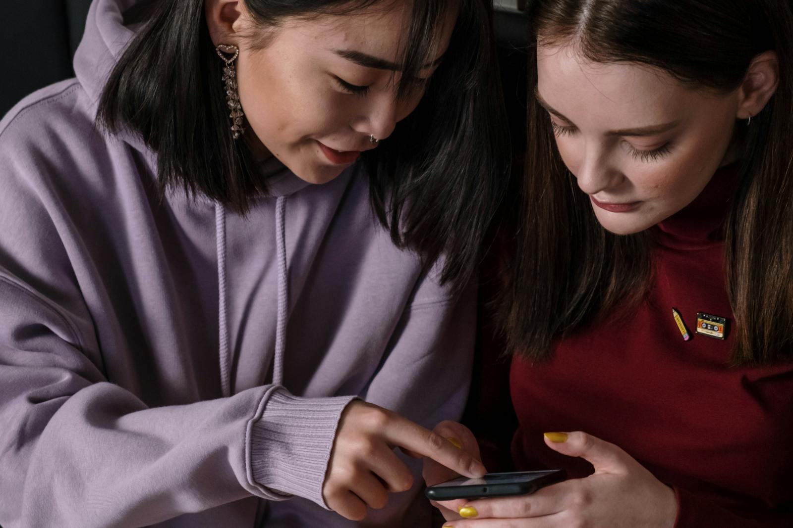 Two teenage girls looking at a smartphone screen together indoors.