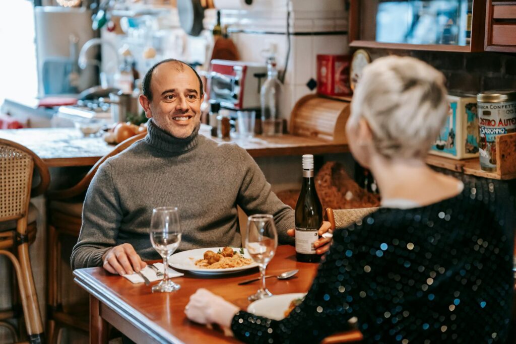 Couple enjoying a romantic dinner with wine in a cozy restaurant setting, sharing smiles and good food.