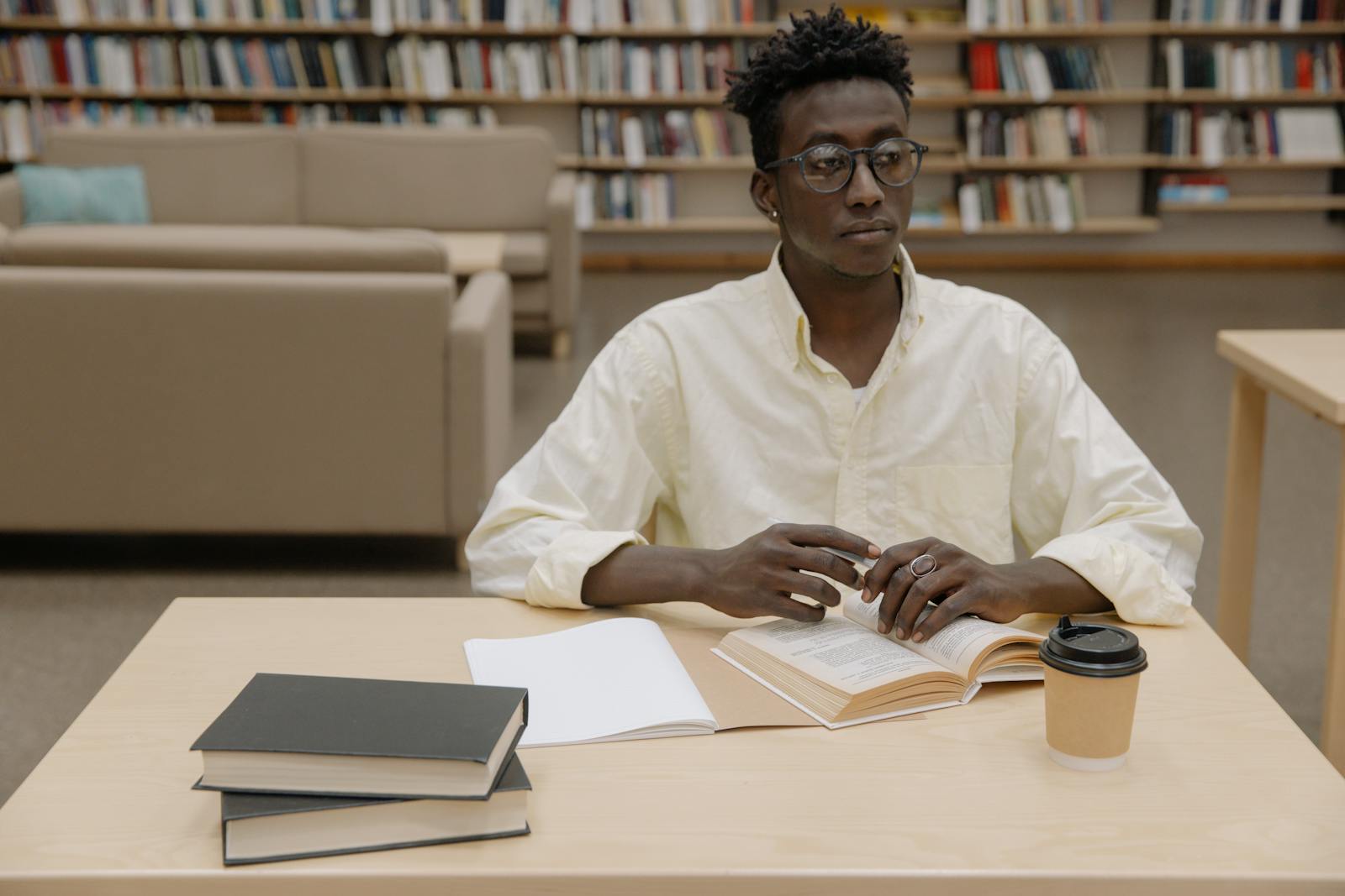 Young man intensely studying in a library setting, surrounded by books.