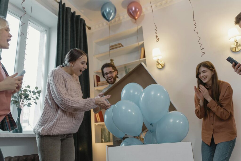Friends joyfully celebrate a gender reveal with blue balloons indoors.