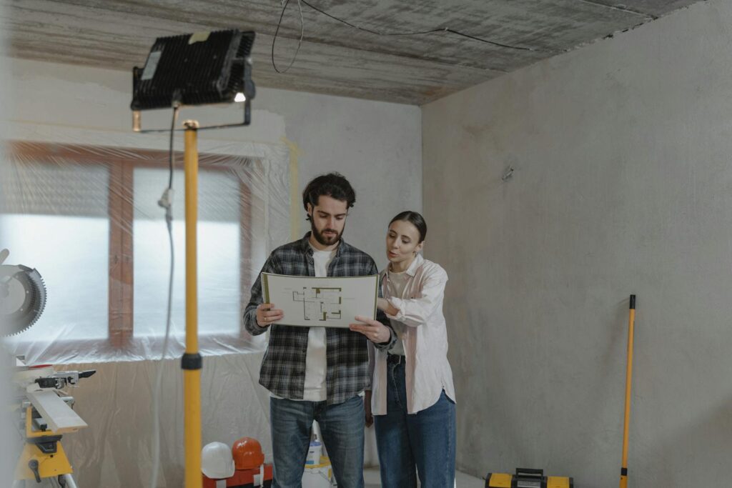 A couple examines blueprints in a partially renovated room, planning home improvements.