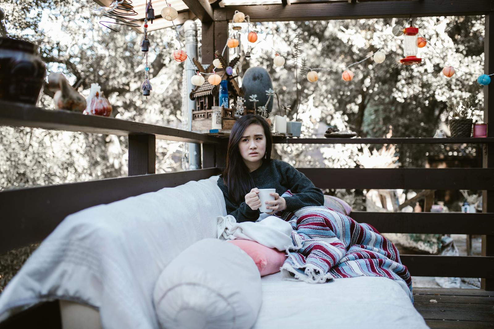 Woman enjoying a quiet afternoon with tea on a patio, wrapped in a colorful blanket.