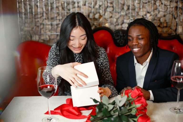 A joyful couple sharing a heartfelt gift at a romantic dinner setting with red roses and wine.