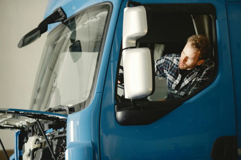 A mechanic checks the engine of a blue truck indoors, focusing on maintenance.
