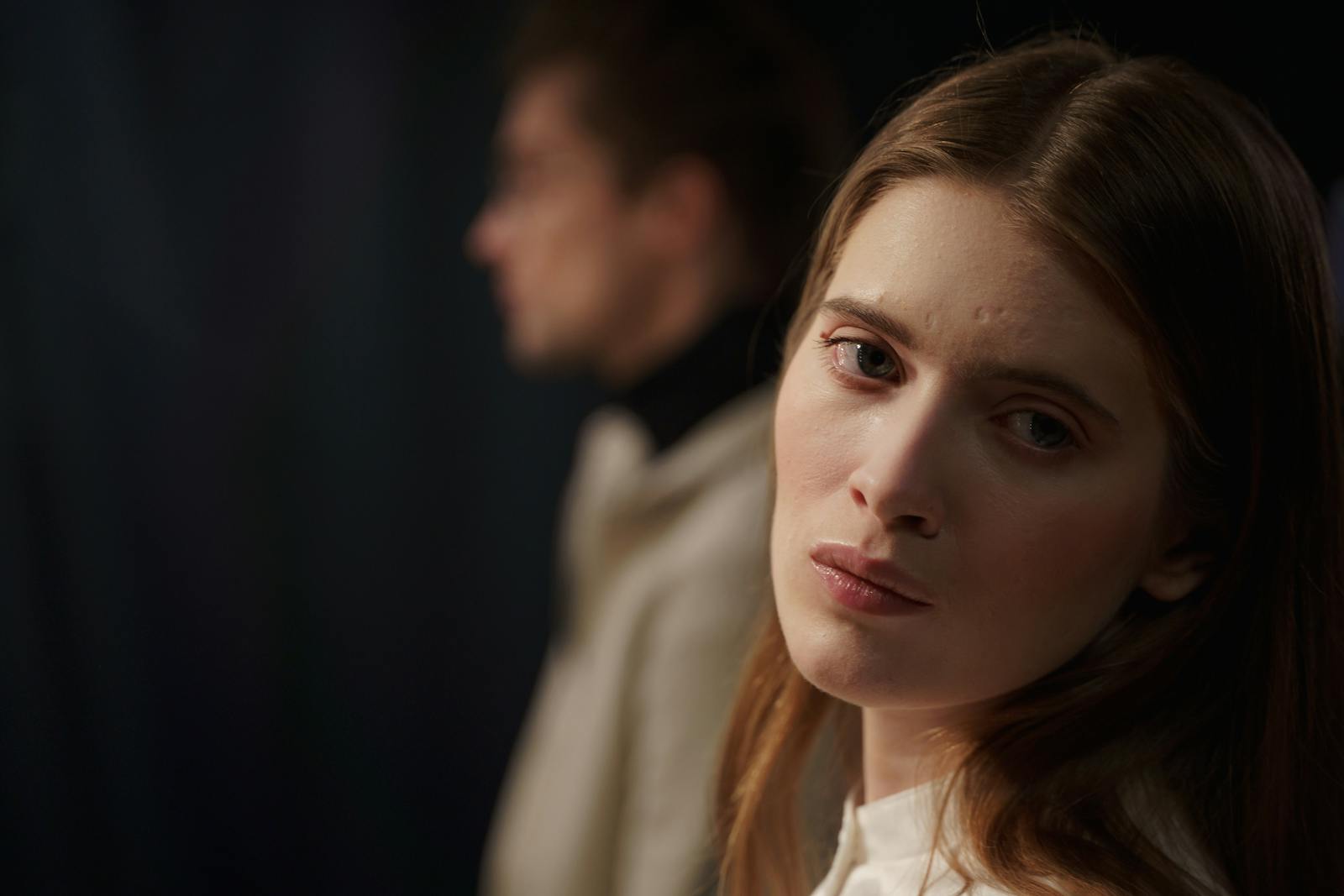 Close-up indoor portrait of a young woman displaying emotions, with a blurred background.