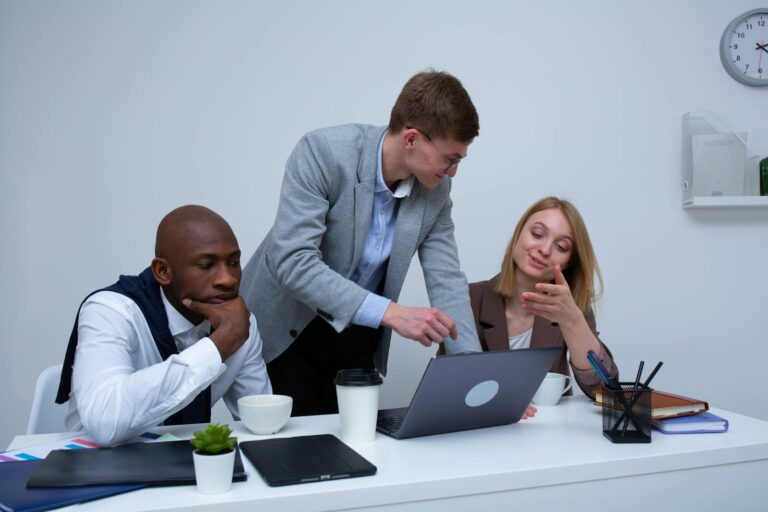 A diverse team collaborating in a modern office environment, discussing work on a laptop.