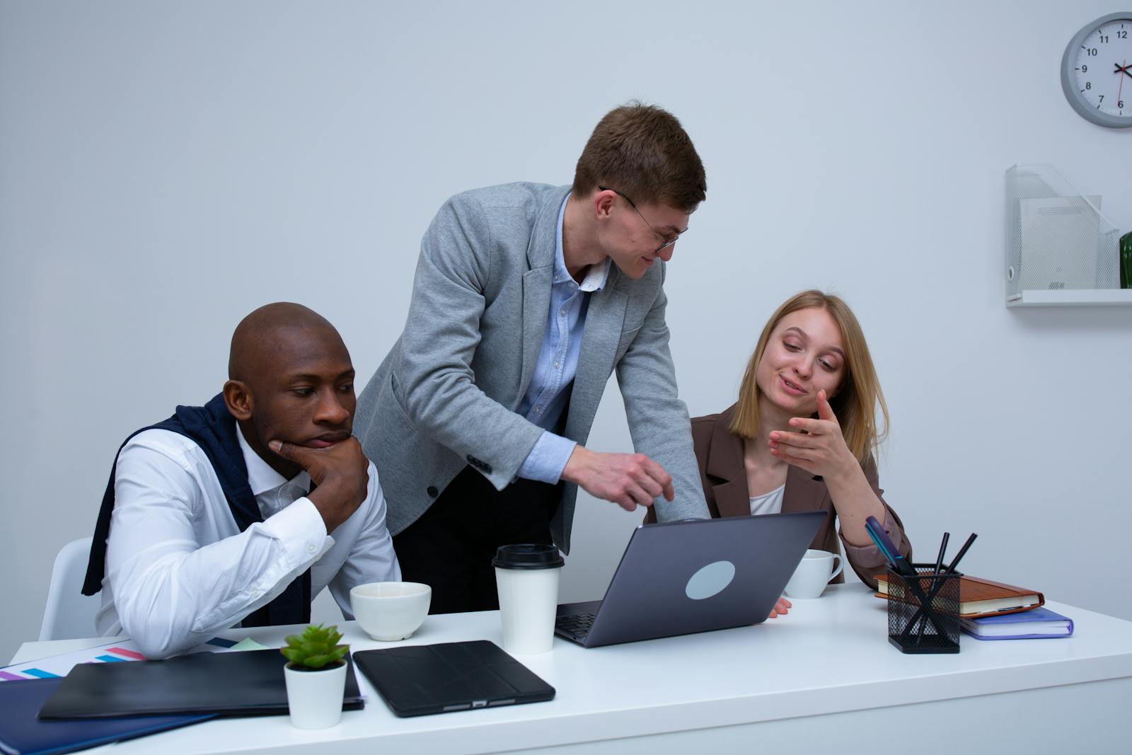 A diverse team collaborating in a modern office environment, discussing work on a laptop.