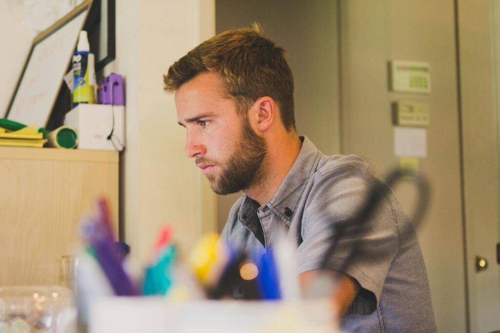 A young man with a beard intensely working at a desk in an office environment.