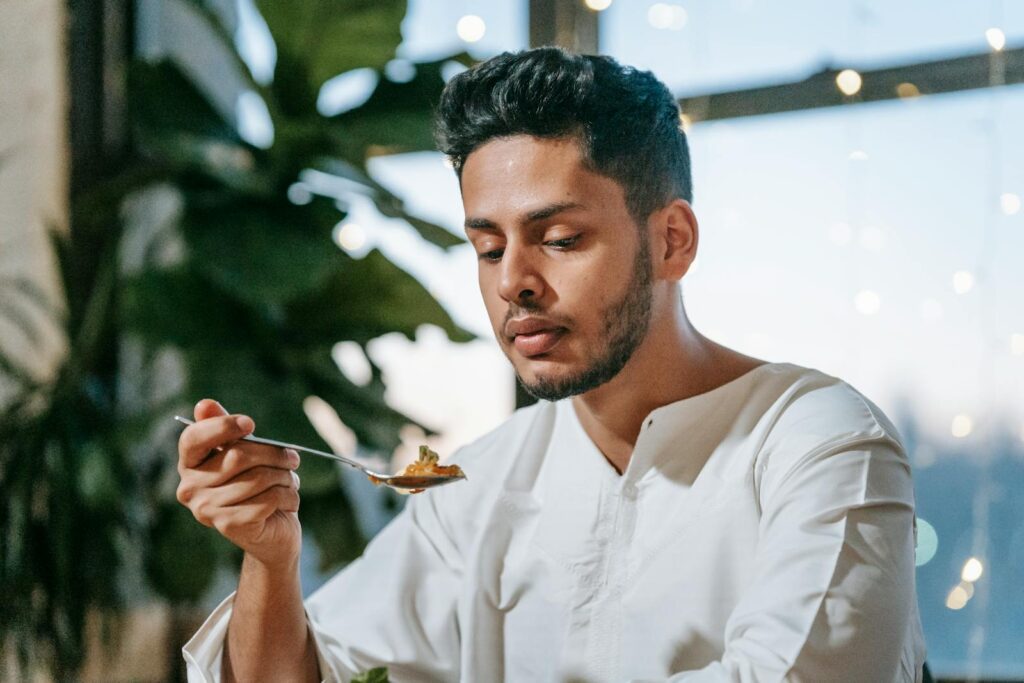 A man in traditional Islamic clothing eating indoors with string lights decor.