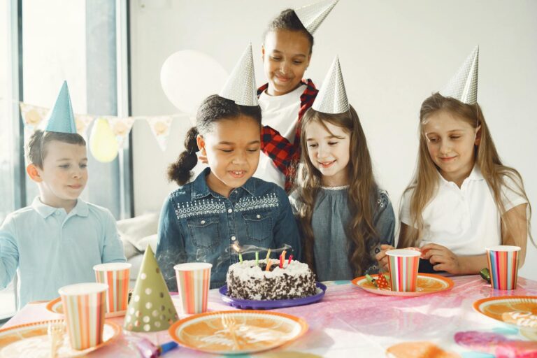 A group of diverse kids celebrating a birthday with cake and party hats.