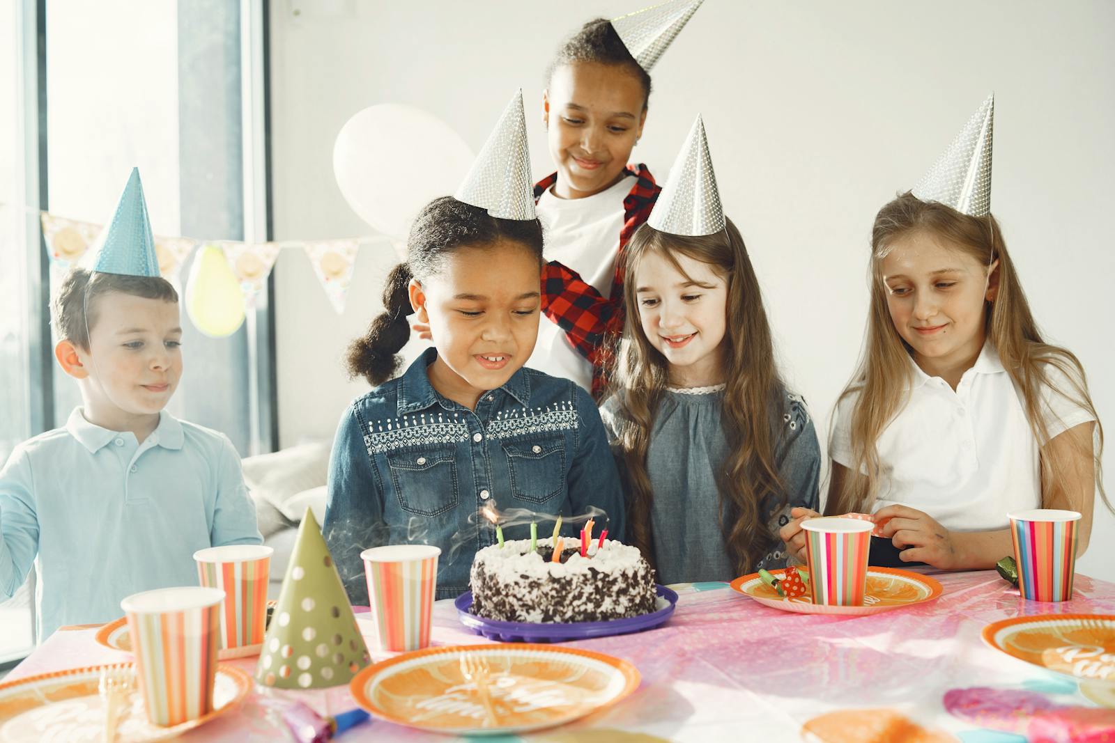 A group of diverse kids celebrating a birthday with cake and party hats.