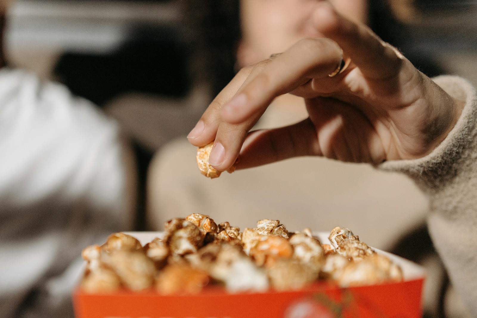 A hand reaches for a piece of popcorn in a cinema setting, creating a cozy atmosphere.