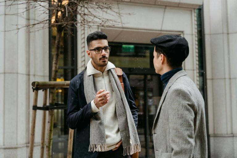 Two businessmen engaged in conversation outside in winter attire with snow falling lightly.