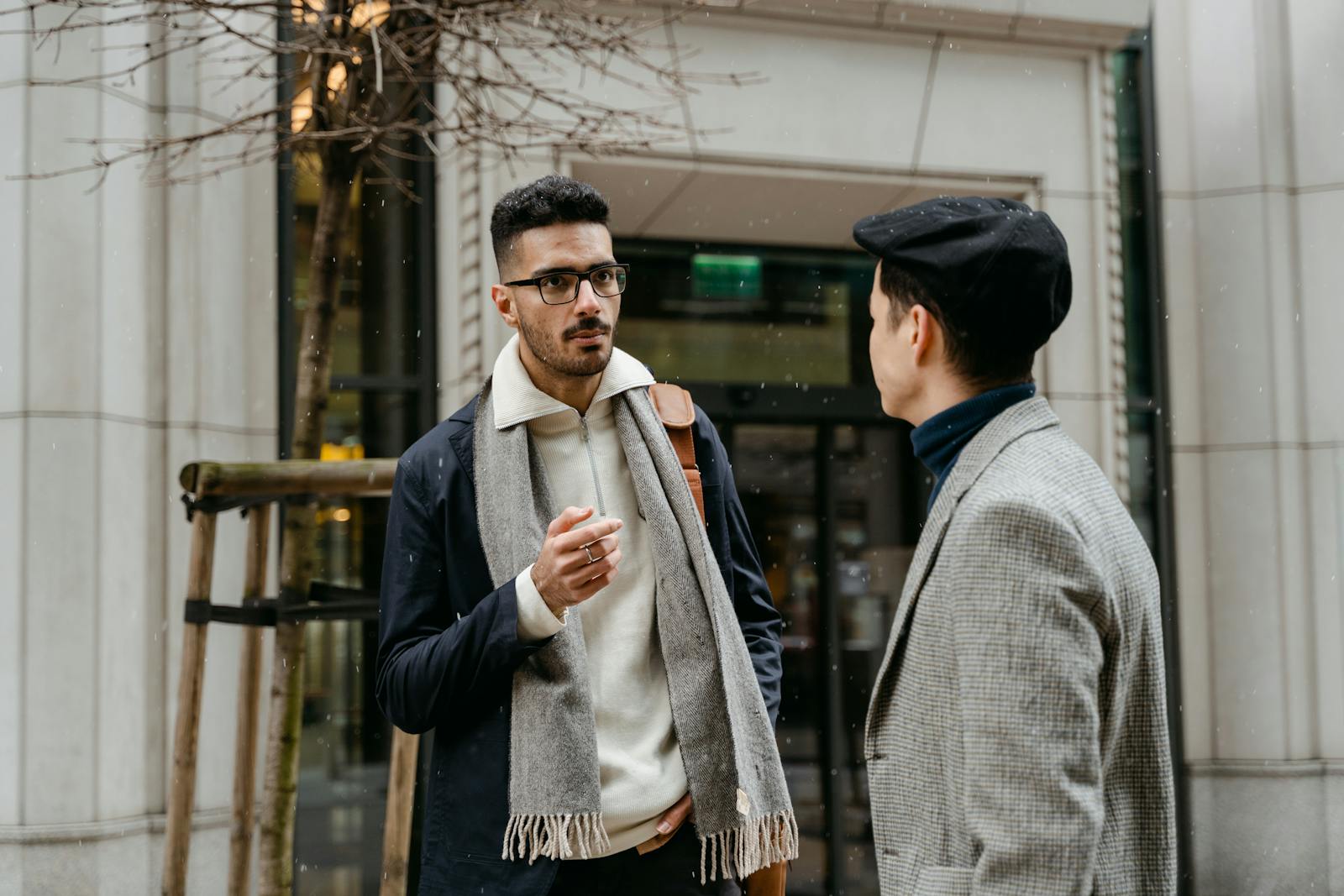 Two businessmen engaged in conversation outside in winter attire with snow falling lightly.