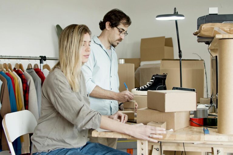 Business partners organizing inventory in an online store setup with clothes and boxes.