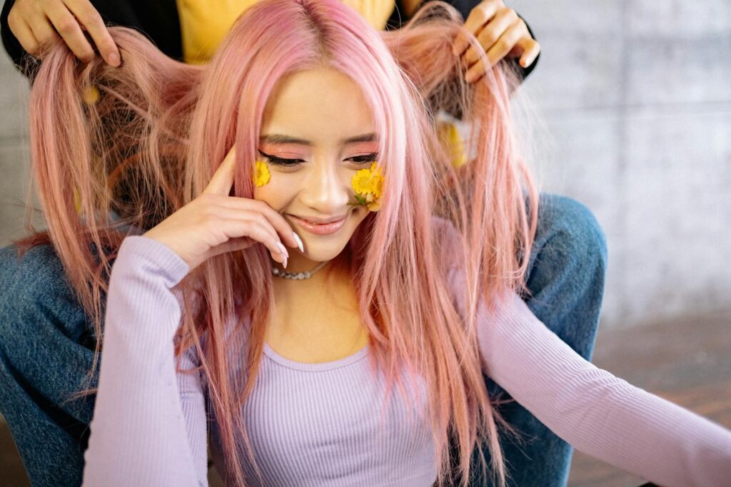 Vibrant portrait of a young woman with pink hair and creative makeup, smiling.