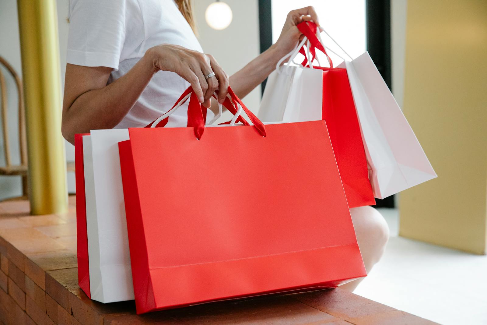 Side view of crop anonymous female buyer in white t shirt sitting on bench with many shopping bags in daylight