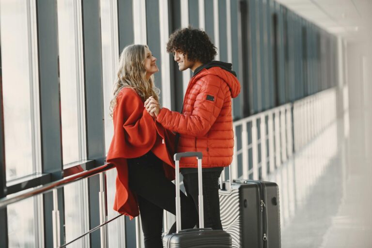 A cheerful couple holding hands with luggage in an airport terminal, ready for travel.