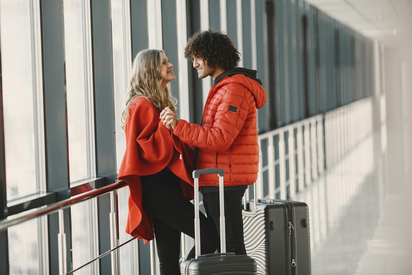 A cheerful couple holding hands with luggage in an airport terminal, ready for travel.