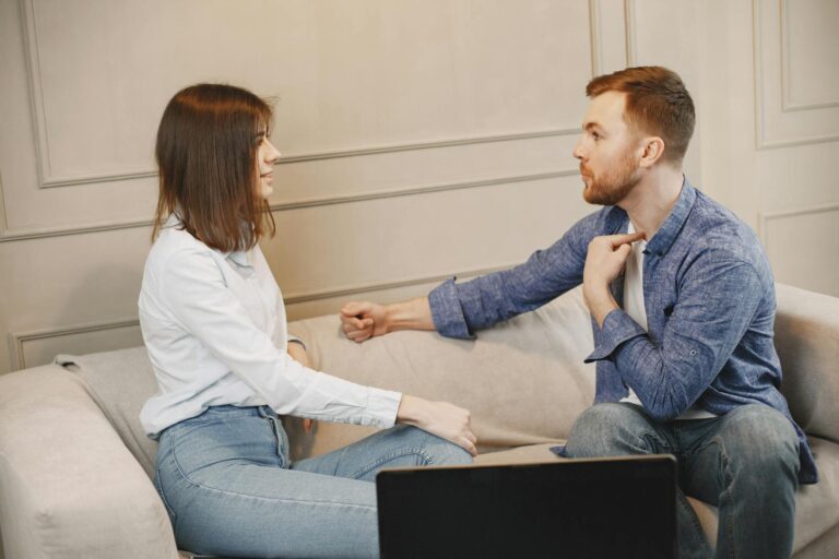 A young couple engaged in a conversation while sitting on a beige couch indoors.