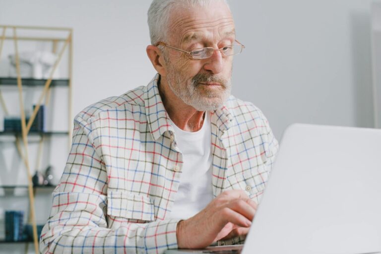 Senior man with eyeglasses working on a laptop in a modern indoor setting.