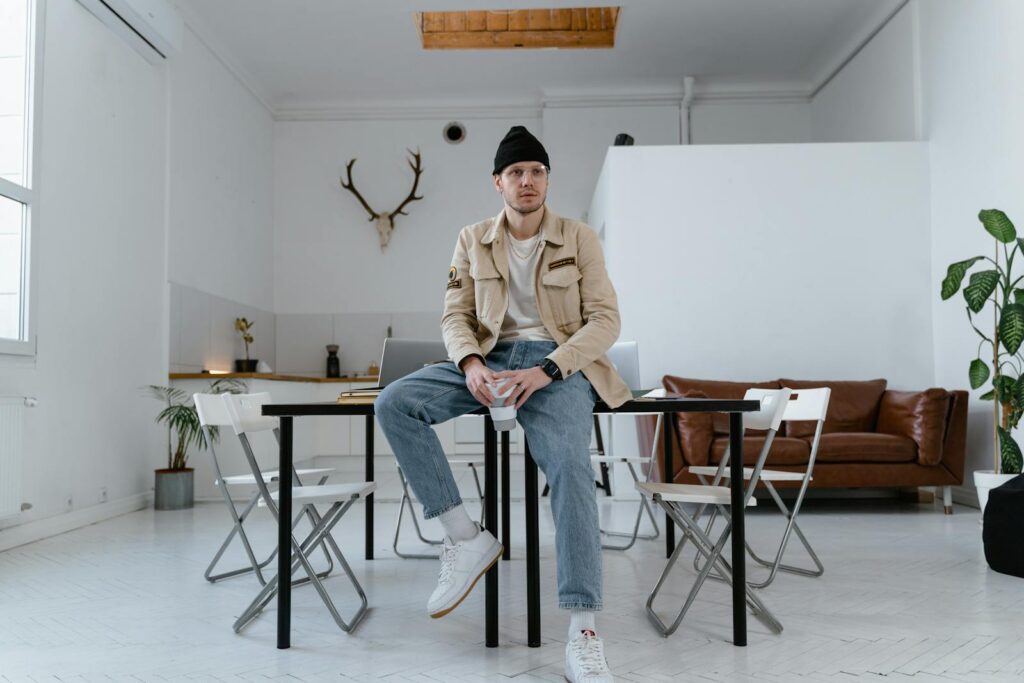 Bearded man in casual attire sitting in a minimalist living room with modern decor.