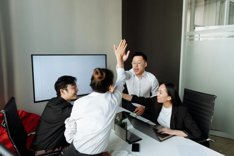 A group of Asian colleagues high-fiving in an office during a business meeting, showcasing teamwork and success.