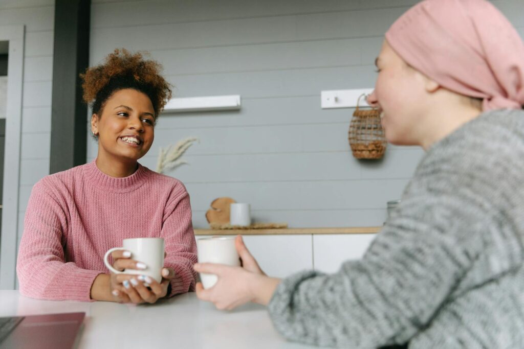 Two women share a joyful coffee moment at home, embodying friendship and warmth.