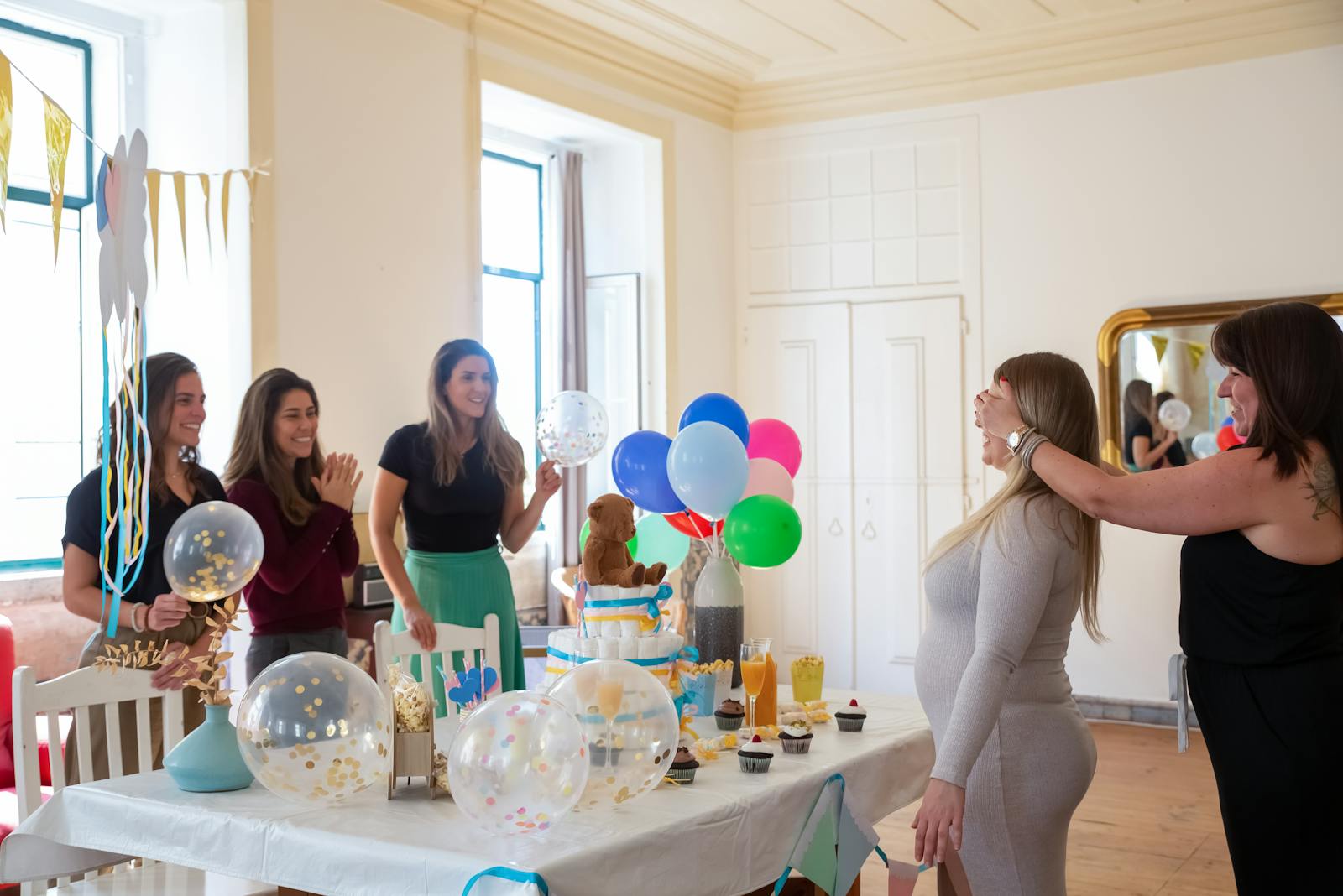 Pregnant woman celebrates joyful baby shower with friends, balloons, and gifts indoors.