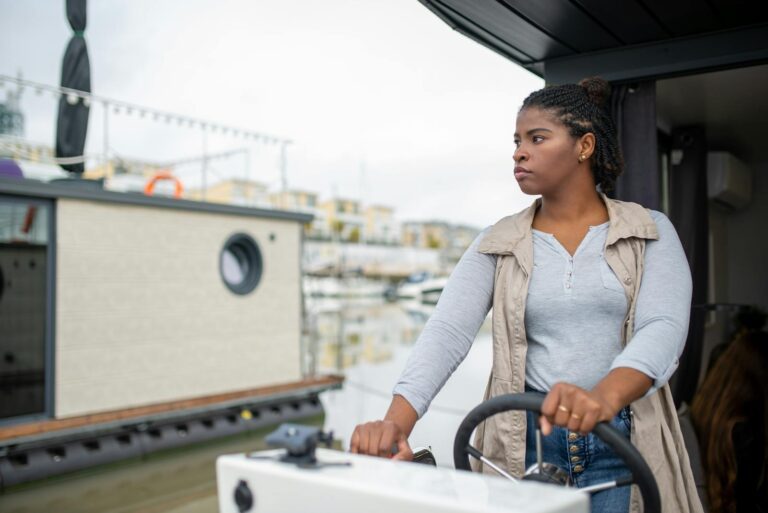 Confident young woman steering a boat in a picturesque Portuguese harbor, enjoying a leisurely day at sea.