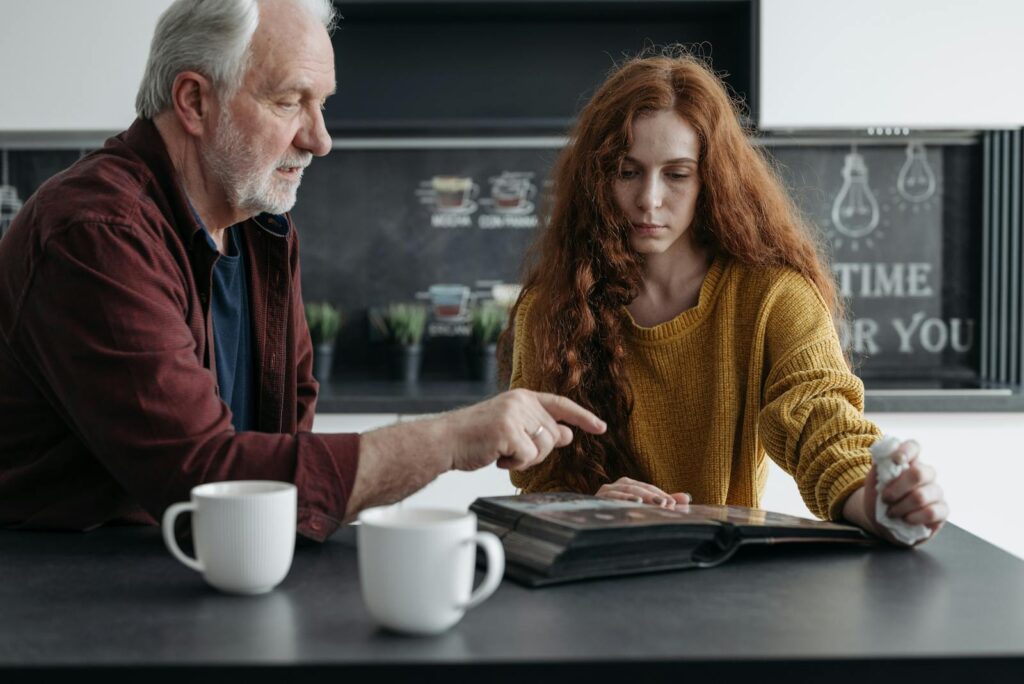 Elderly man and young woman share a poignant moment reminiscing over a photo album.